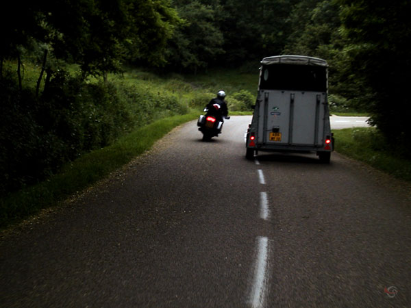 motorcycle rider passes horse trailer just before a corner