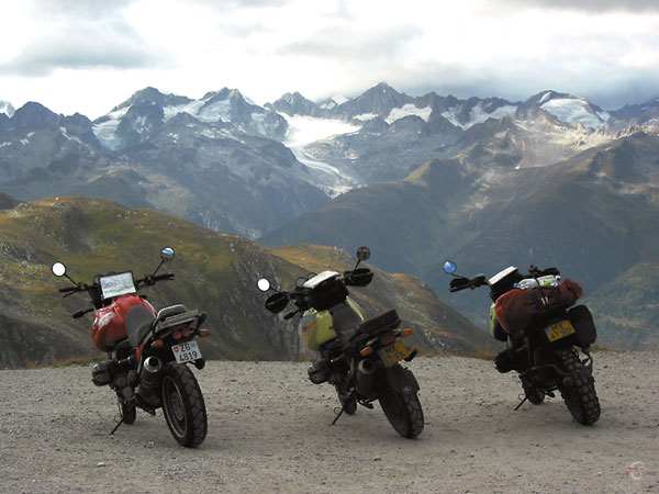Three motorcycles with a view on the Alps, parked at the rim of an abyss