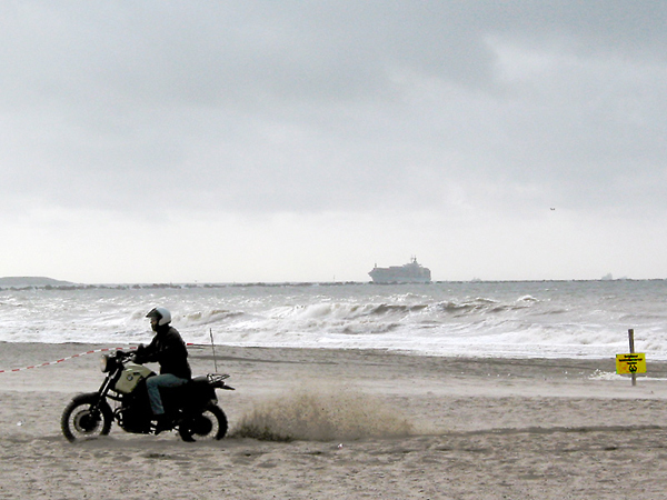 Motorcycle rider through the sand (much sand behind him)