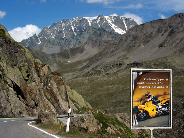 Big sign in the snowy Alps, showing a motorcyclist and the words Prudence, Vorsicht, Prudenza
