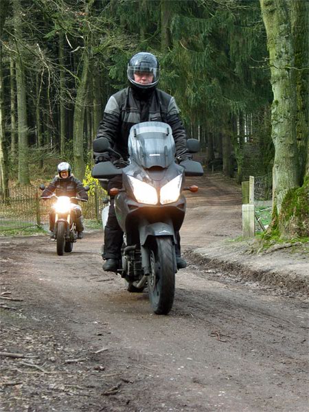 Two motorcycle ridiers on an unpaved road